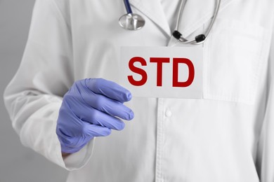 Doctor holding sheet of paper with abbreviation STD on grey background, closeup