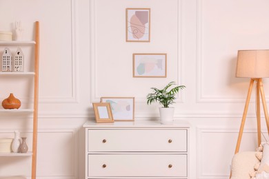 Photo of Picture frames hanging on white wall and chest of drawers at home