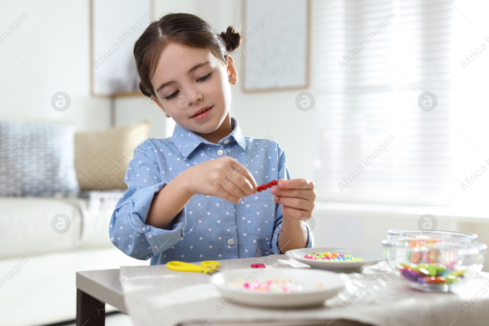 Photo of Little girl making accessory with beads at table indoors. Creative hobby