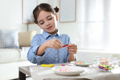 Little girl making accessory with beads at table indoors. Creative hobby