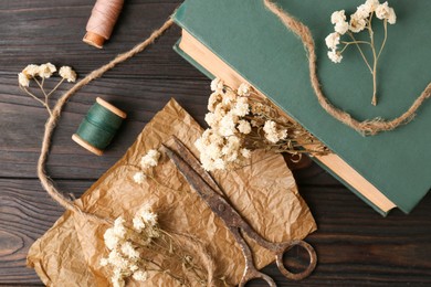 Flat lay composition of book with flowers as bookmark and scissors on wooden table