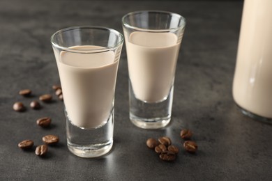 Photo of Coffee cream liqueur in glasses and beans on grey table, closeup