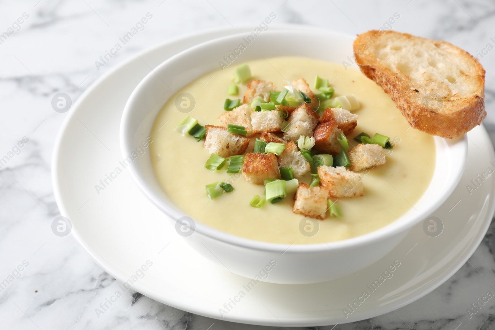 Photo of Tasty potato soup with croutons and green onion in bowl on white marble table