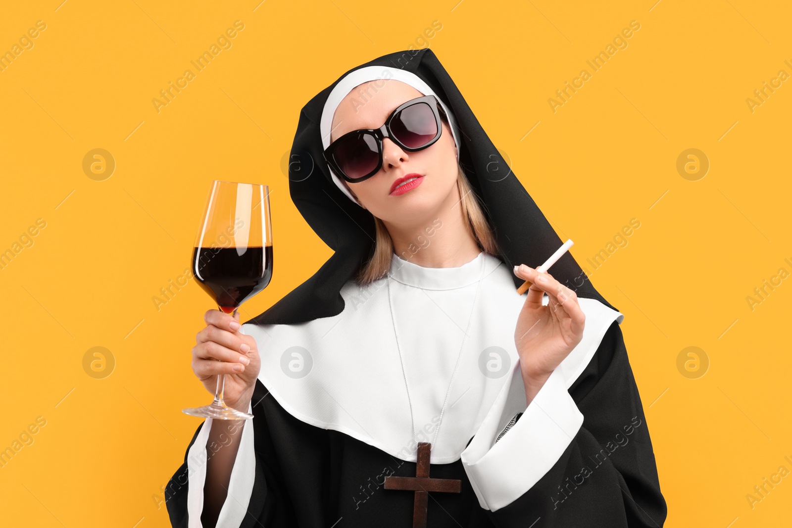 Photo of Woman in nun habit holding glass of wine and cigarette against orange background