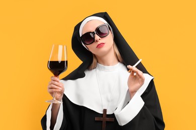 Photo of Woman in nun habit holding glass of wine and cigarette against orange background