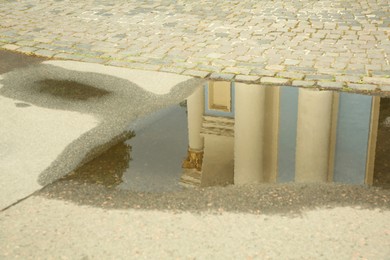 Reflection of beautiful building in puddle on asphalt