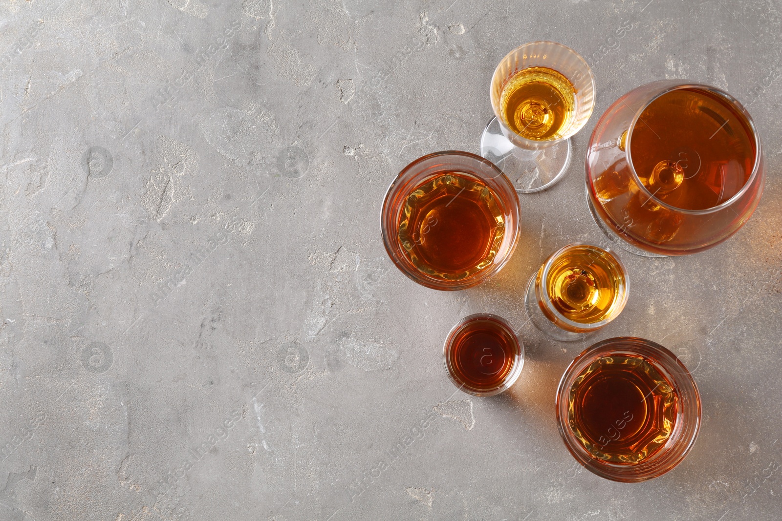 Photo of Different delicious liqueurs in glasses on grey table, flat lay. Space for text