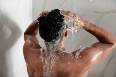 Photo of Man washing hair in shower at home, back view
