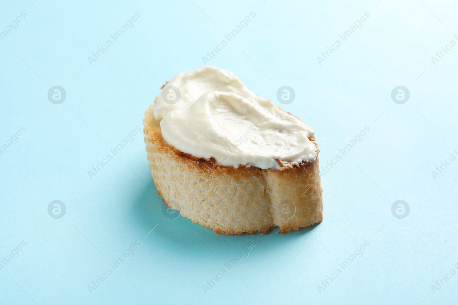 Photo of Piece of baguette with tasty cream cheese on color background