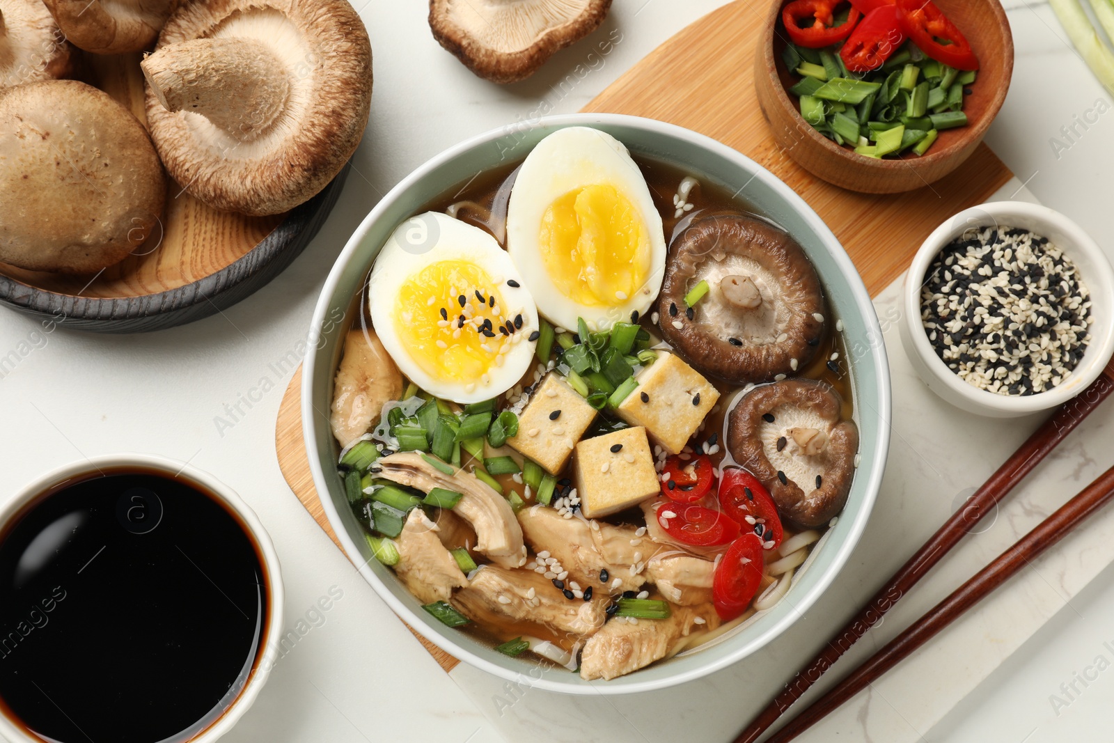 Photo of Bowl of delicious ramen and ingredients on white table, flat lay. Noodle soup