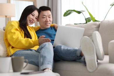 Happy couple with laptop on sofa at home