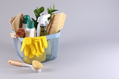 Photo of Set of different cleaning supplies in basket on light grey background. Space for text