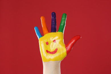 Photo of Kid with smiling face drawn on palm against red background, closeup