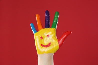 Kid with smiling face drawn on palm against red background, closeup