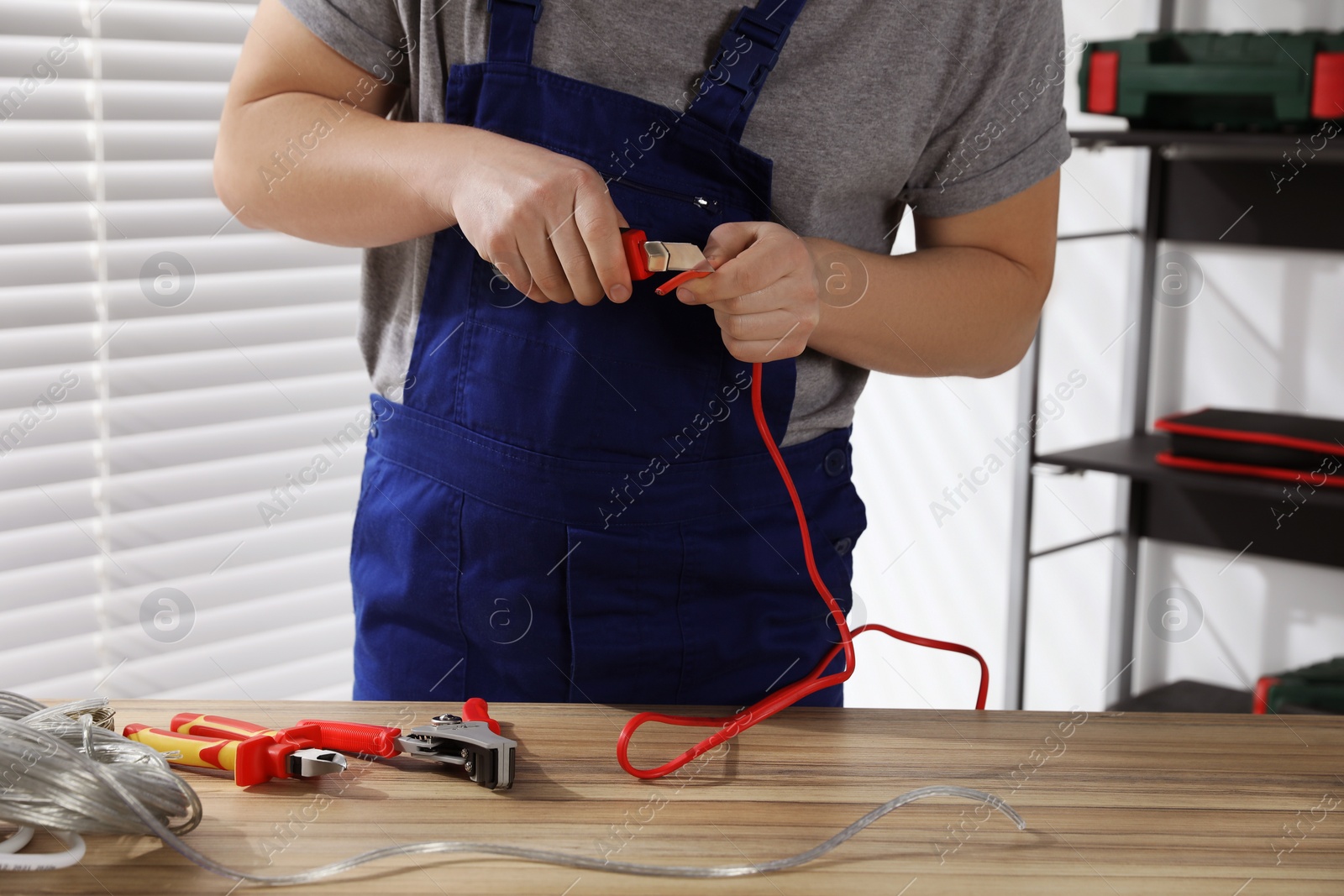 Photo of Professional electrician in uniform stripping wiring indoors, closeup