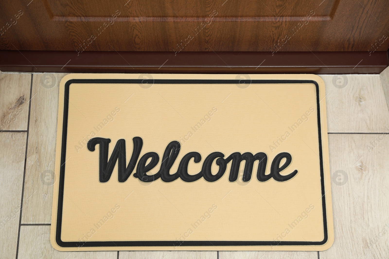 Photo of Beautiful beige doormat with word Welcome on floor near entrance, top view