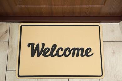 Photo of Beautiful beige doormat with word Welcome on floor near entrance, top view