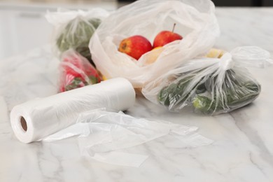 Photo of Plastic bags with different fresh products on white marble table