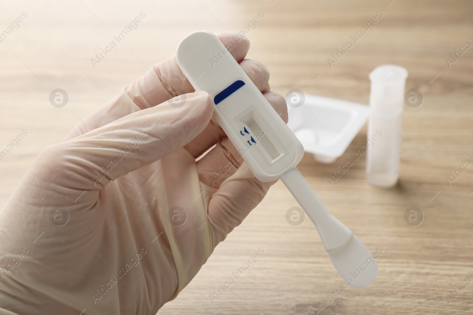 Photo of Woman holding disposable express test above wooden table, closeup