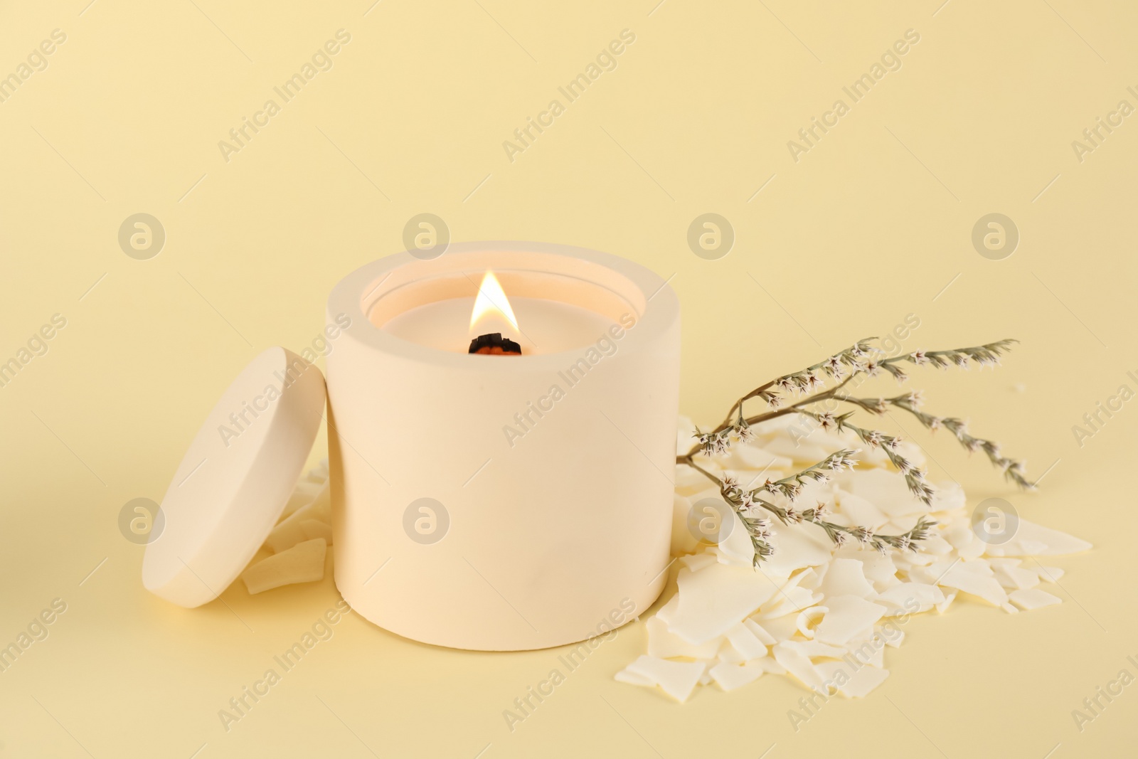 Photo of Burning soy candle, wax flakes and statice twig on beige background
