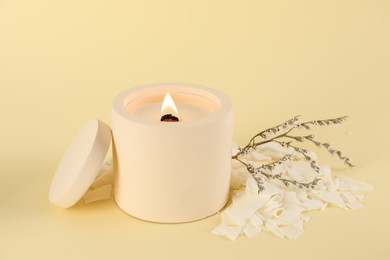 Photo of Burning soy candle, wax flakes and statice twig on beige background
