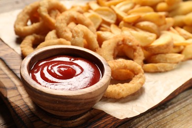 Bowl tasty ketchup and different snacks on wooden table, closeup