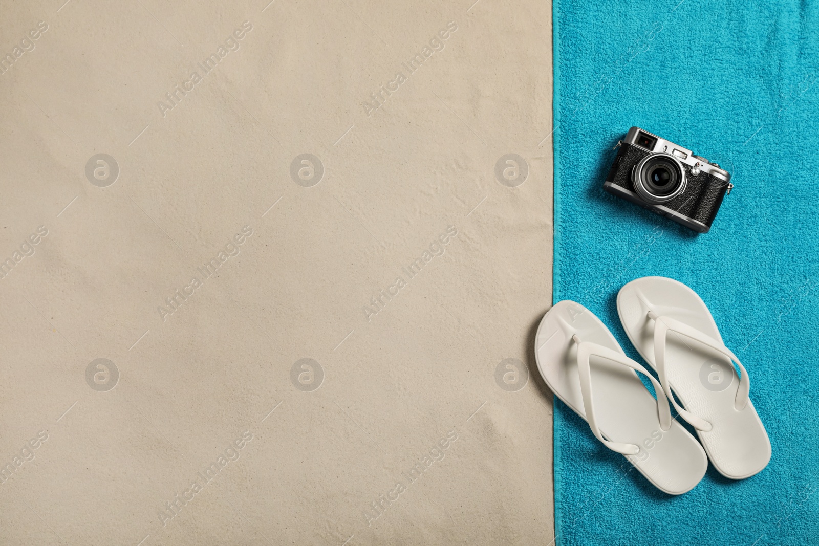 Photo of Beach towel, camera and flip flops on sand, top view. Space for text