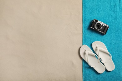 Beach towel, camera and flip flops on sand, top view. Space for text