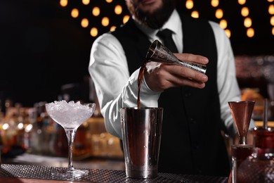 Bartender preparing fresh alcoholic cocktail in martini glass at bar counter, closeup