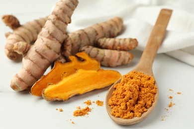 Photo of Wooden spoon with aromatic turmeric powder and raw roots on white table, closeup