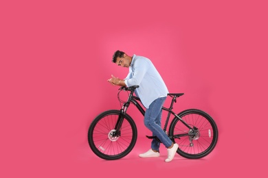 Photo of Handsome young man with modern bicycle on pink background
