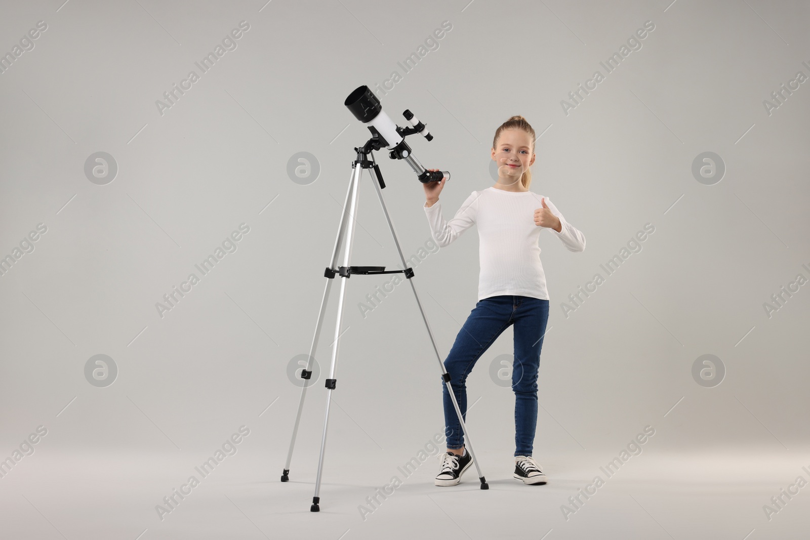 Photo of Happy little girl with telescope showing thumb up on light grey background