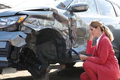 Photo of Insurance agent filling claim form near broken car outdoors