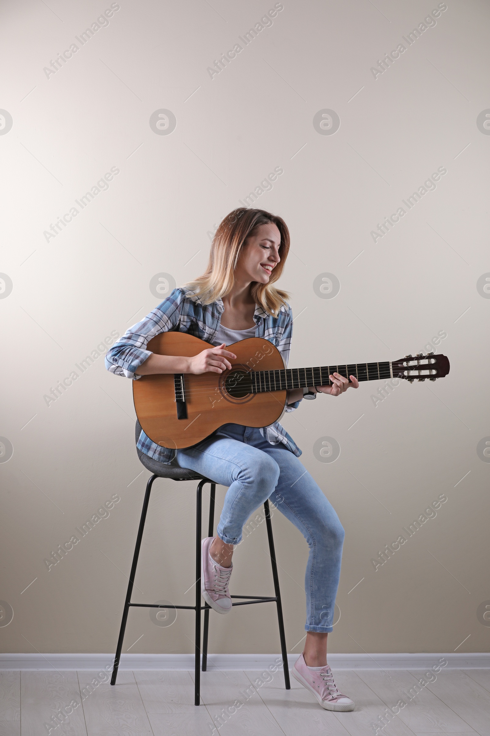 Photo of Young woman playing acoustic guitar near grey wall