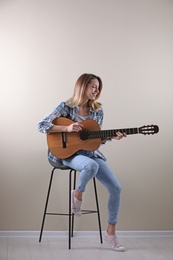 Young woman playing acoustic guitar near grey wall