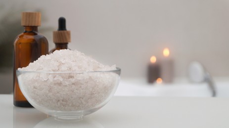 Photo of Glass bowl with bath salt and cosmetic products on white countertop indoors, space for text