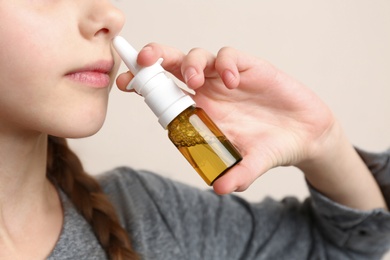 Photo of Sick little girl using nasal spray on beige background, closeup