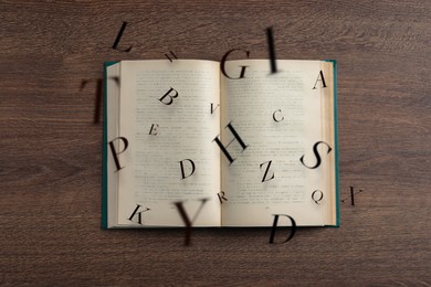 Image of Open book with letters flying out of it on wooden background, top view