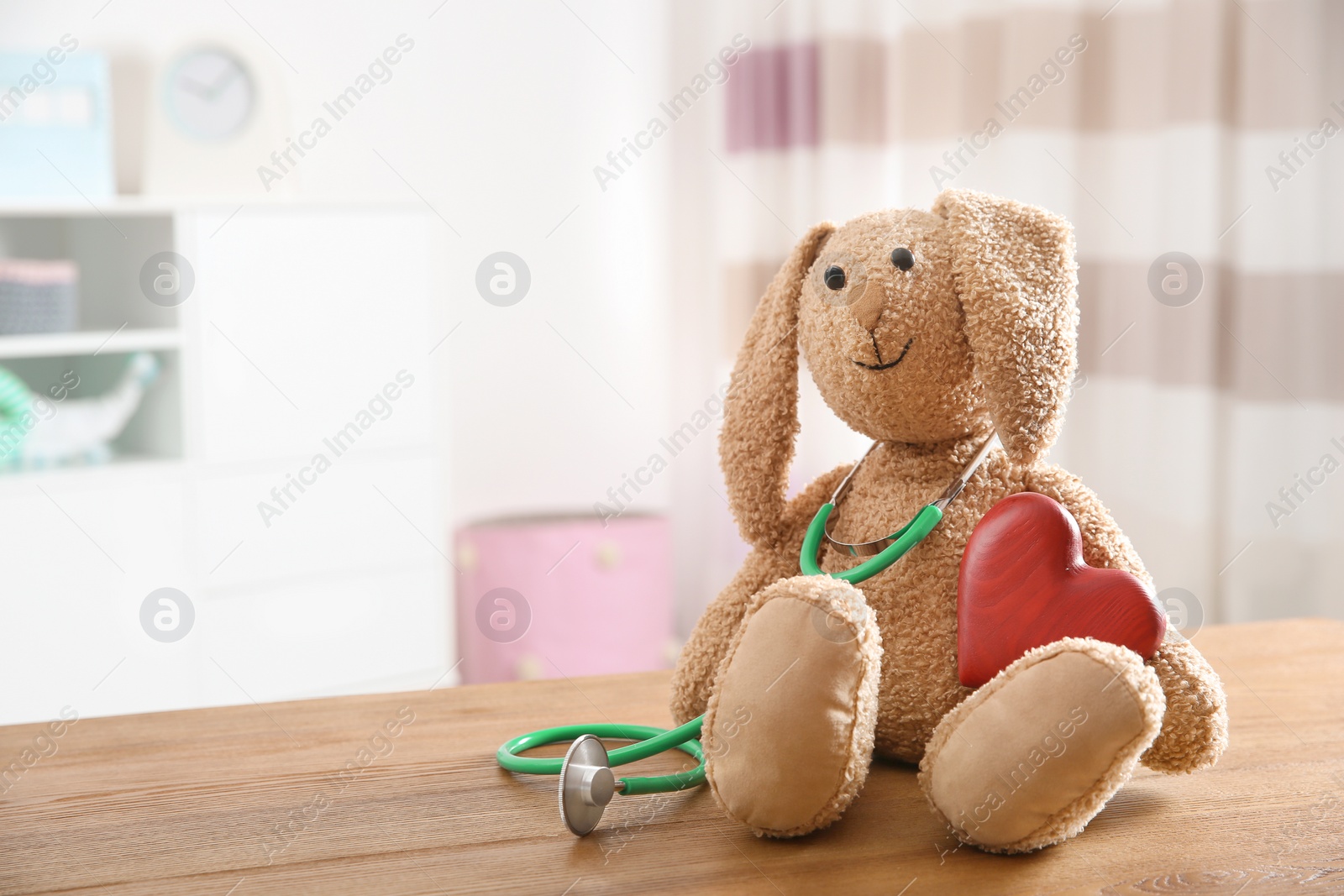 Photo of Toy bunny, stethoscope and heart on table indoors, space for text. Children's doctor