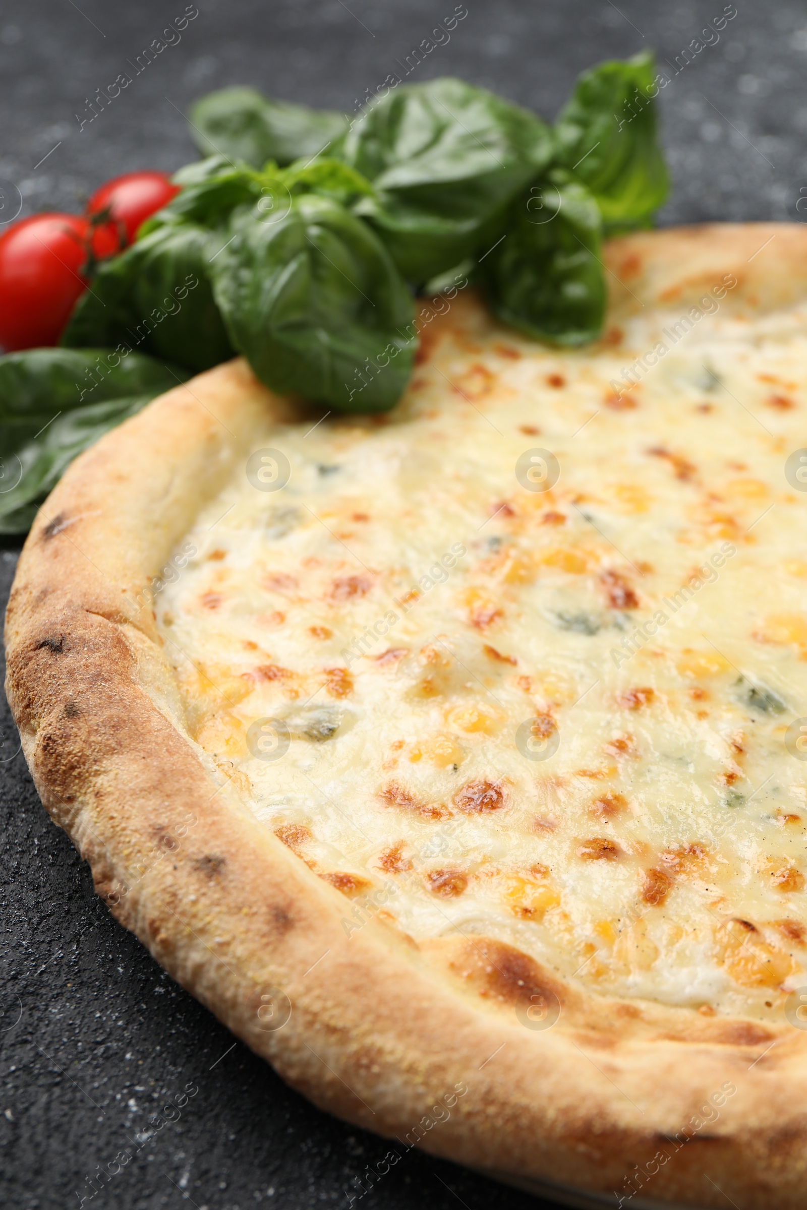 Photo of Delicious cheese pizza, basil and tomatoes on black textured table, closeup