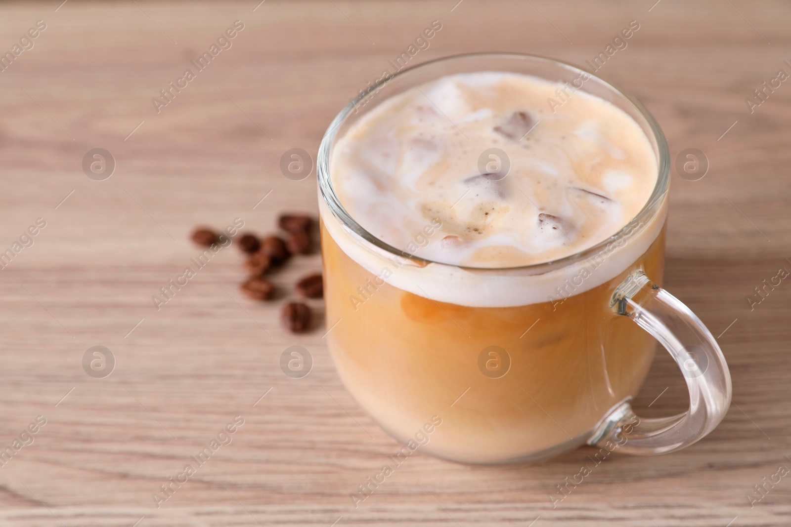 Photo of Cup of fresh iced coffee and beans on wooden table, closeup. Space for text