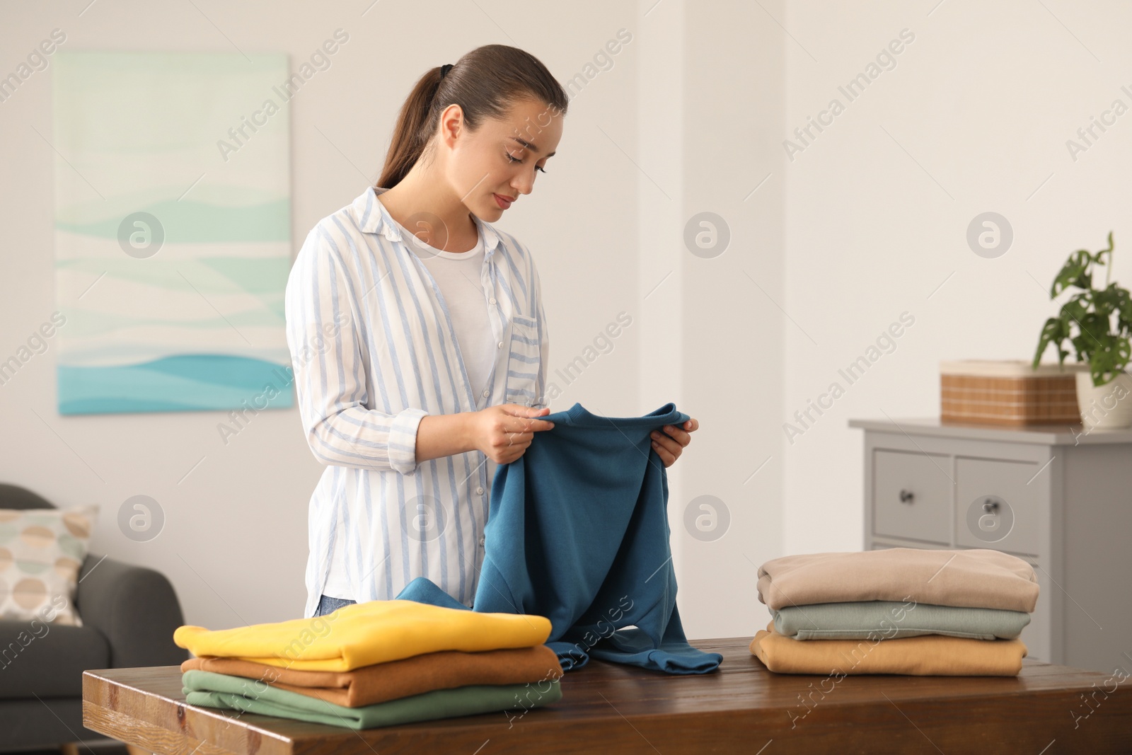 Photo of Young woman folding clothes at wooden table indoors