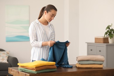 Photo of Young woman folding clothes at wooden table indoors
