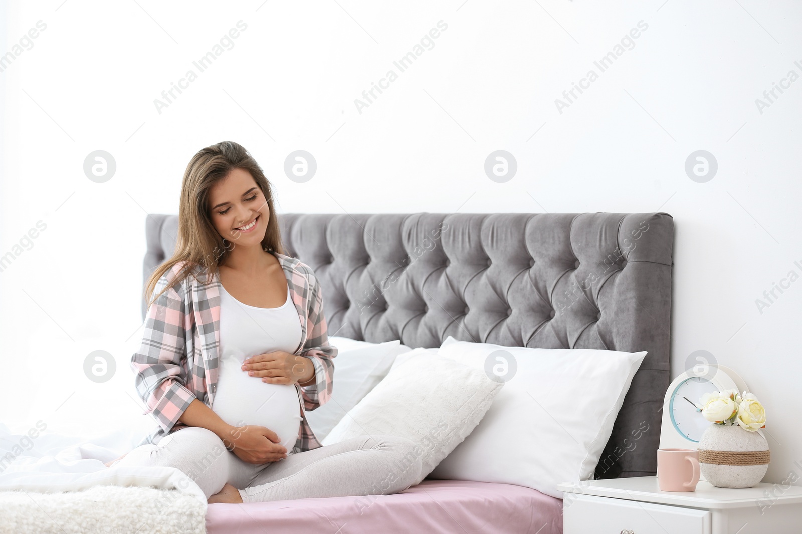 Photo of Happy pregnant woman sitting on bed at home