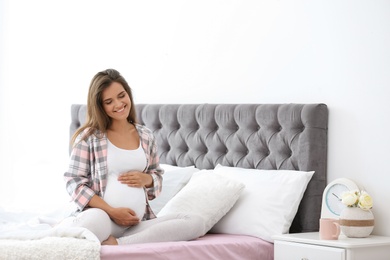 Photo of Happy pregnant woman sitting on bed at home