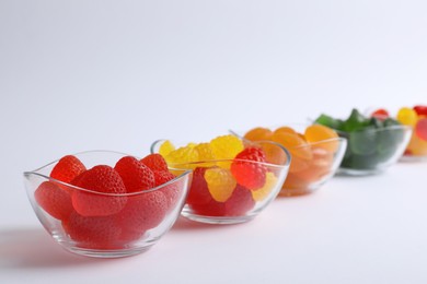 Different delicious gummy candies in bowls on white background