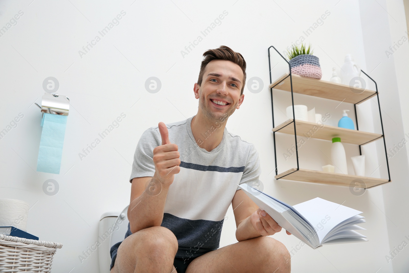 Photo of Young man with book sitting on toilet bowl in bathroom