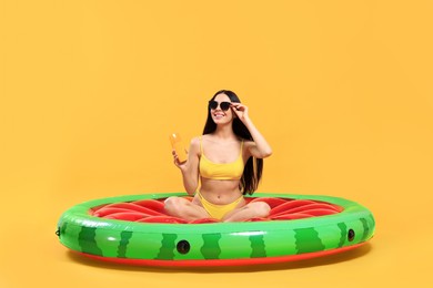 Photo of Happy young woman with sunscreen bottle on inflatable mattress against orange background. Seasonal suntan