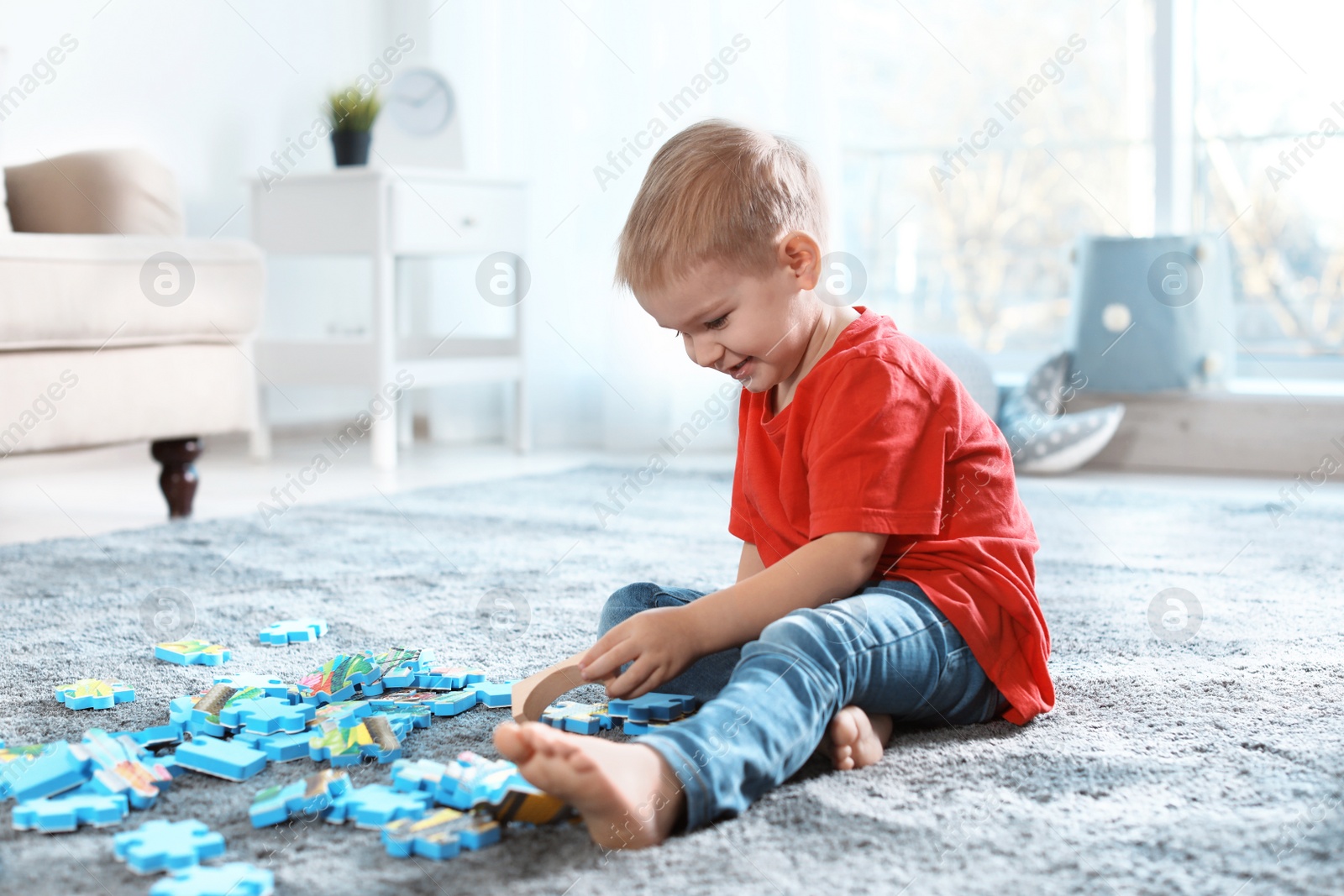 Photo of Cute little child playing with puzzles on floor indoors