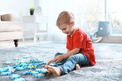 Cute little child playing with puzzles on floor indoors